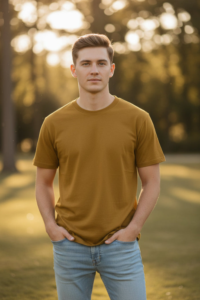 A man wearing a solid mustard yellow short-sleeve crewneck t-shirt and light blue jeans, shown from the chin down against a plain white background.