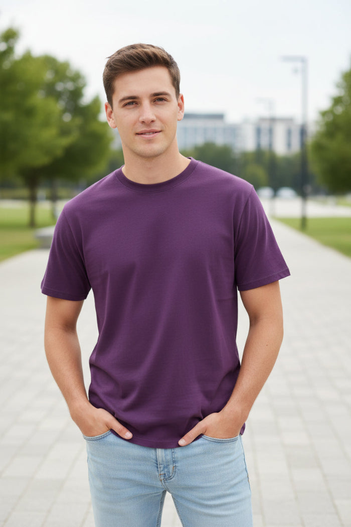 A man wearing a solid purple short-sleeve crewneck t-shirt and light blue jeans, shown from the chin down against a plain white background.