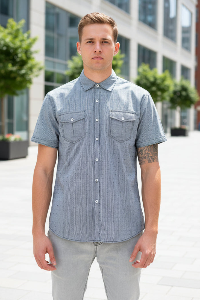A man wearing a light gray short-sleeve button-up shirt with two chest pockets, shown from the neck down against a plain white background.