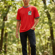 A man wearing a red short-sleeve t-shirt with black and white trim on the collar and cuffs, featuring the green and white Mexican national team crest on the left chest.