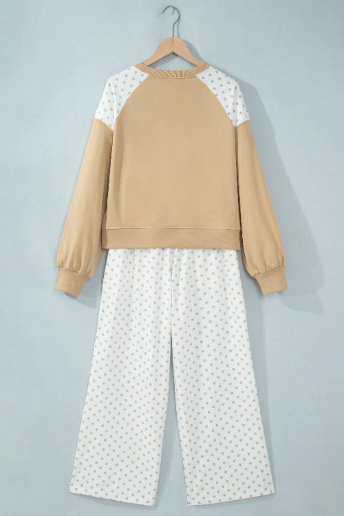 A two-piece pajama set hanging on a wooden hanger against a light gray wall. The set features a cropped long-sleeve sweatshirt with a tan body and white sleeves 