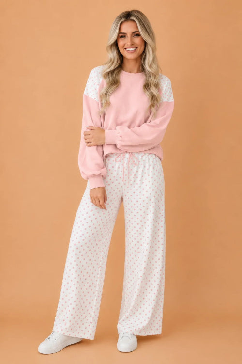 A woman modeling a two-piece loungewear set consisting of a light pink long-sleeve sweatshirt with white lace shoulder panels and white wide-leg 