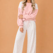 A woman modeling a two-piece loungewear set consisting of a light pink long-sleeve sweatshirt with white lace shoulder panels and white wide-leg 