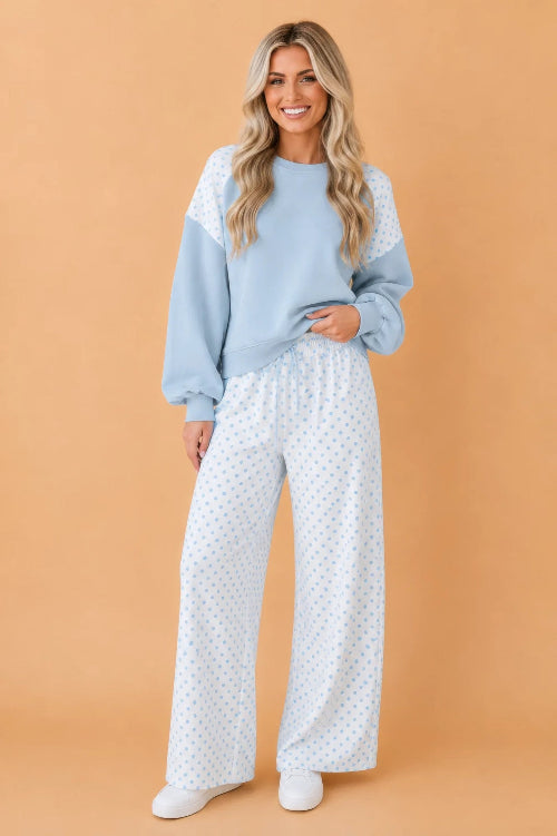 A woman modeling a light blue crewneck sweatshirt with white lace shoulder panels and matching white wide-leg pants 