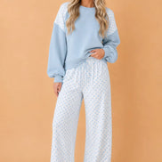 A woman modeling a light blue crewneck sweatshirt with white lace shoulder panels and matching white wide-leg pants 