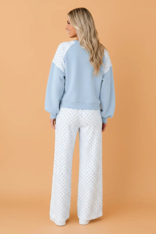A woman shown from the back wearing a light blue and white color-blocked sweatshirt with white wide-leg pants 