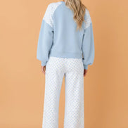 A woman shown from the back wearing a light blue and white color-blocked sweatshirt with white wide-leg pants 
