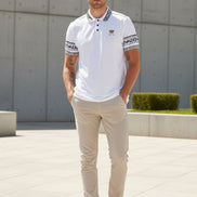 White polo shirt with black and gold details worn by a person on a white background
