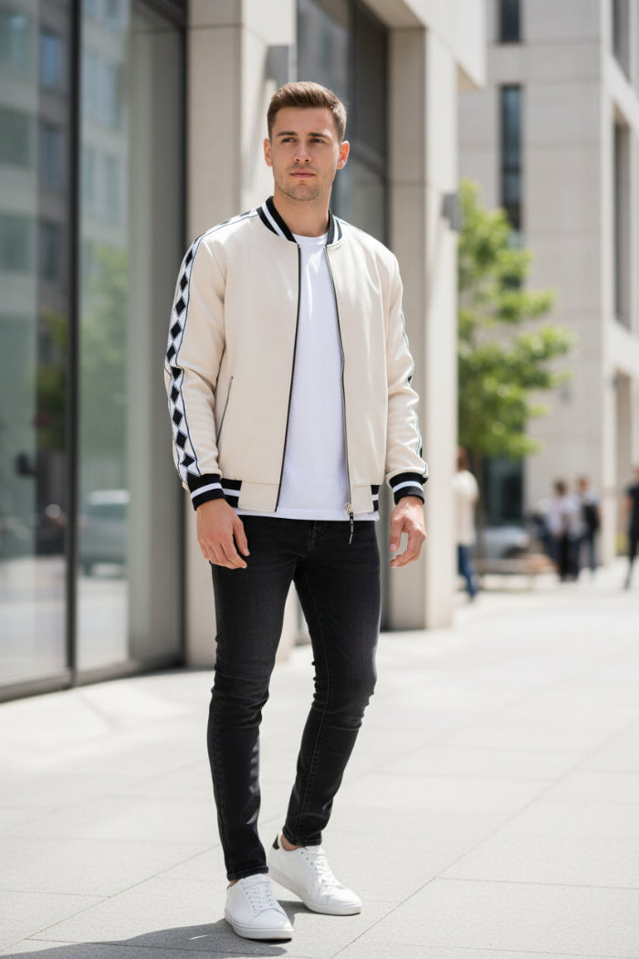 Man wearing a cream bomber jacket with black and white checkered sleeves  outside