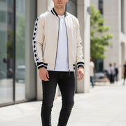 Man wearing a cream bomber jacket with black and white checkered sleeves  outside
