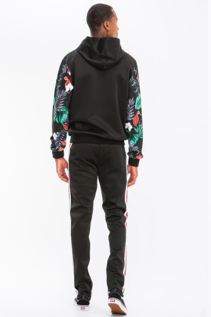 Person wearing a black hoodie with floral sleeves and black pants with white stripes on a white background