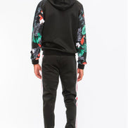 Person wearing a black hoodie with floral sleeves and black pants with white stripes on a white background