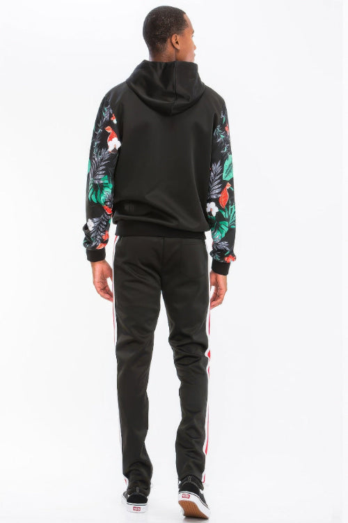 Person wearing a black hoodie with floral sleeves and black pants with white stripes on a white background