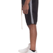 Black shorts with white checkered stripes worn by a person on a white background