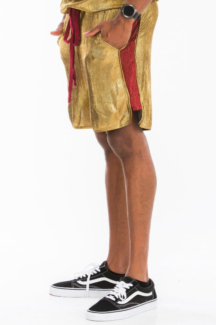 Person wearing gold shorts with red accents and black Vans sneakers on a white background
