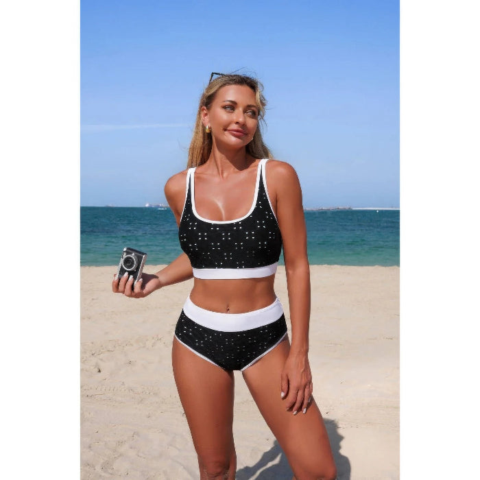 Woman in a black and white bikini standing on a beach with blue water and sky.
