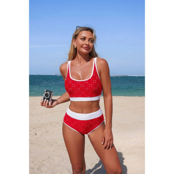 Woman in a red and white swimsuit standing on a beach with blue sky and ocean in the background.