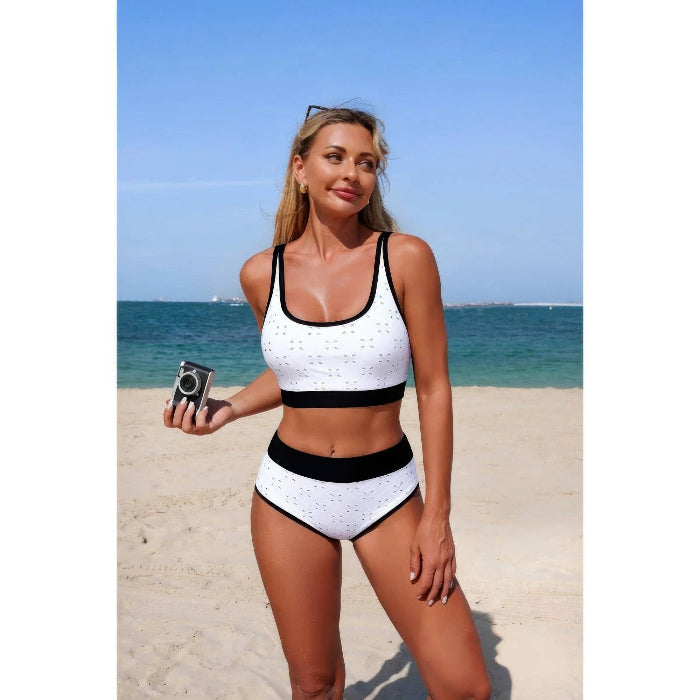 Woman in a black and white swimsuit standing on a beach with blue water and sky.