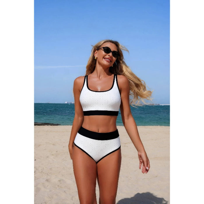 Woman in a white and black swimsuit on a beach with blue sky and ocean.