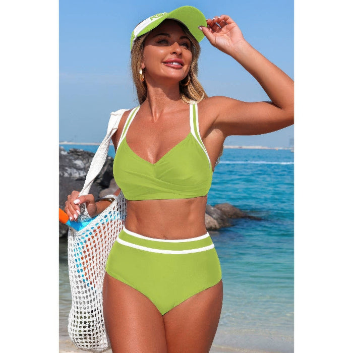 A woman on a beach wearing a bright lime green two-piece bikini with white trim, a matching green visor, and carrying a white mesh tote bag.