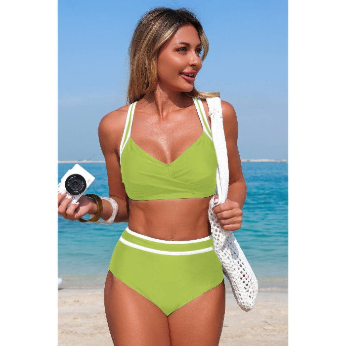 Woman in a green bikini standing on a beach with clear blue water in the background