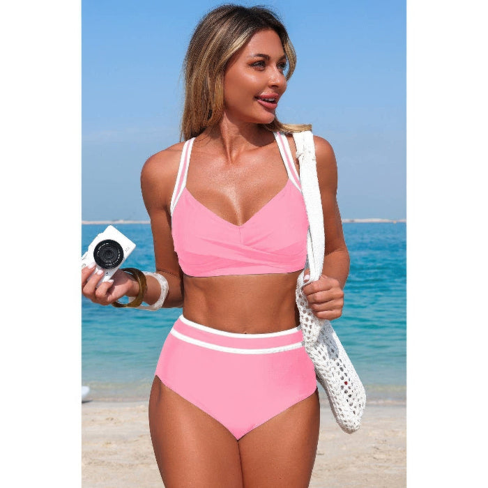 Woman in a pink bikini standing on a beach with clear blue water and sky.