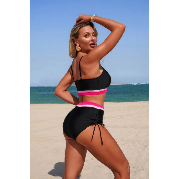 Woman in a black and pink bikini standing on a beach with blue sky and ocean in the background