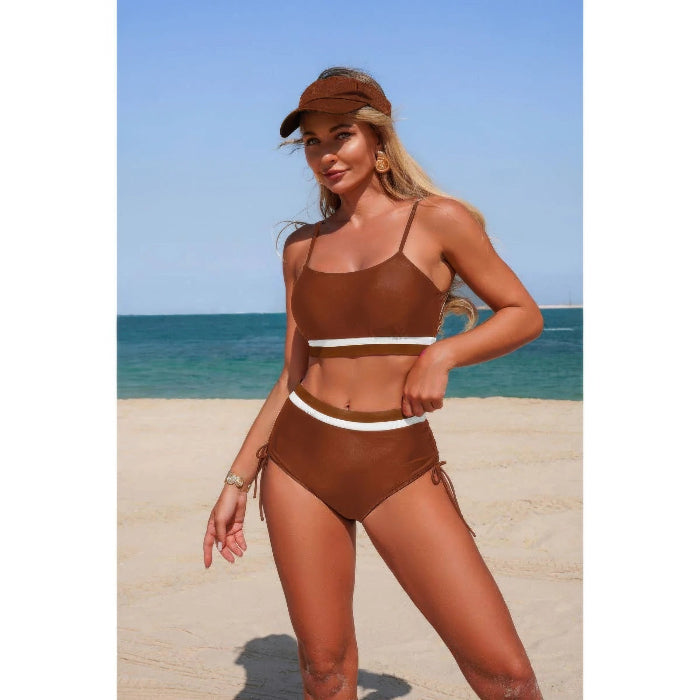 Woman in a brown bikini and visor standing on a beach with clear blue sky.