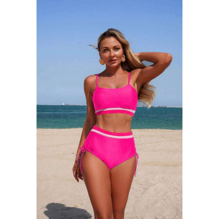 Woman in a pink bikini standing on a beach with blue sky and ocean in the background