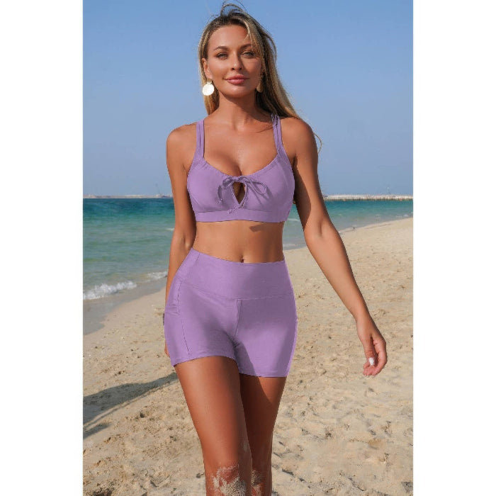 Woman in a purple sports bra and shorts standing on a beach.