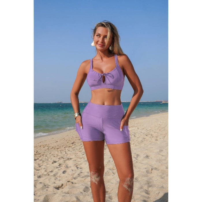 Woman in a purple sports outfit standing on a beach with clear blue sky and ocean.