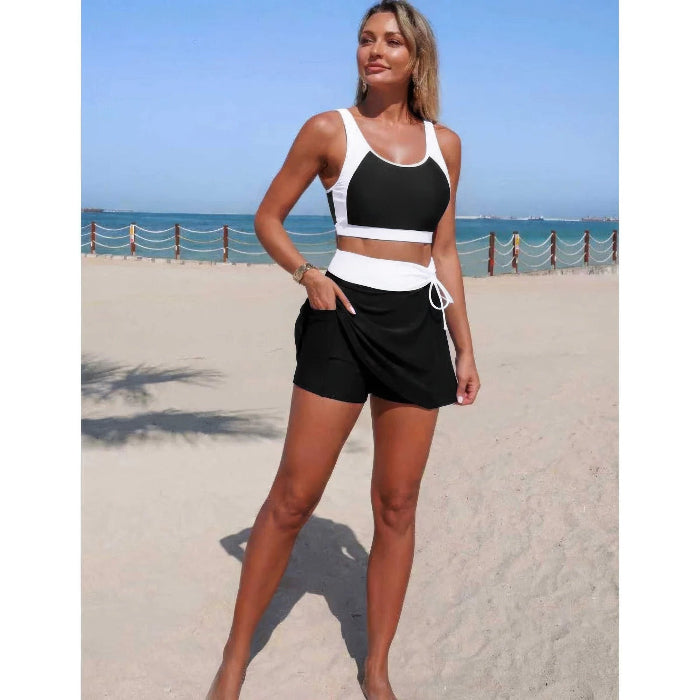 A woman stands on a sandy beach wearing a matching two-piece activewear set consisting of a black and white sports bra and black shorts with a white waist tie.