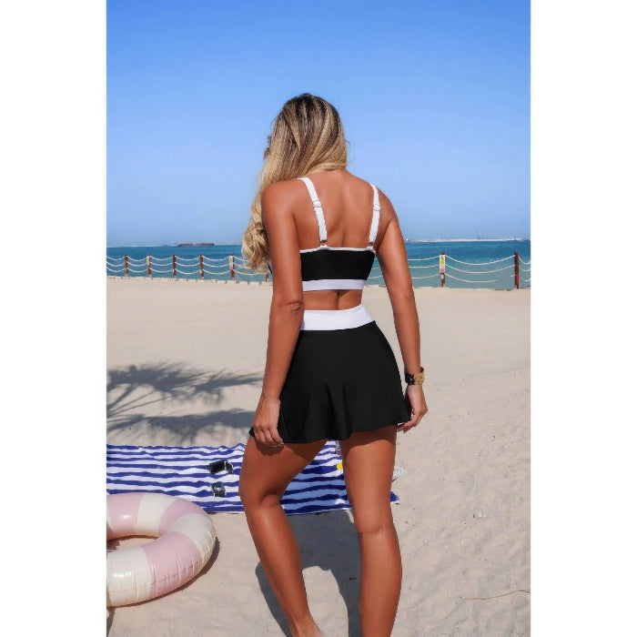 Woman in a black and white bikini top and black skirt on a beach.