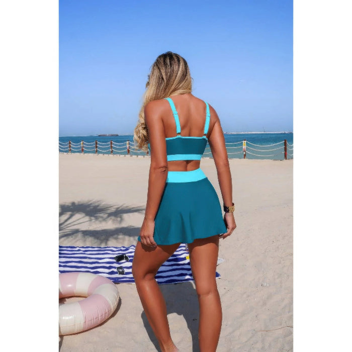 Woman in a blue and green swimsuit on a beach with a clear sky.