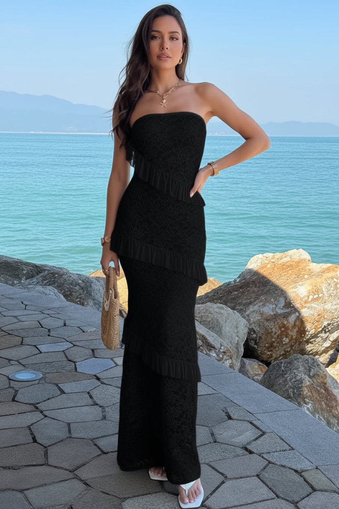 Woman in a black strapless dress standing by a waterfront with rocks and blue water.