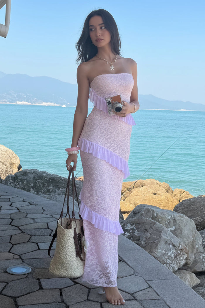 Woman in a pink lace dress standing by a coastal area with blue water and rocks.