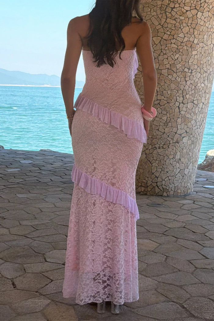 Woman in a pink lace dress standing by a stone wall with ocean view