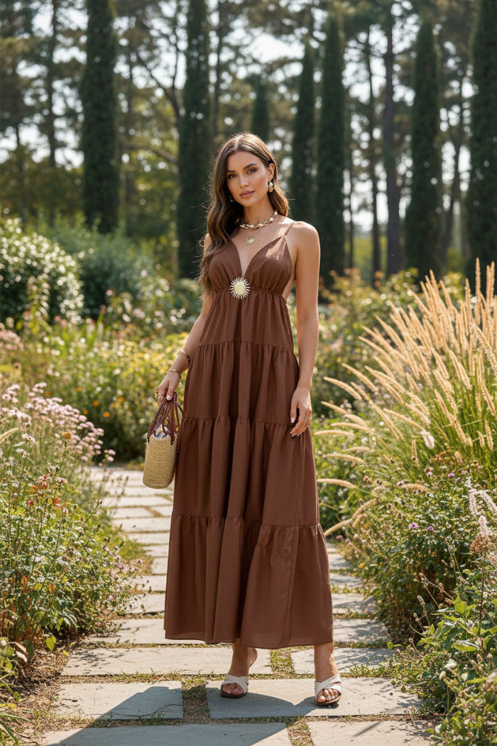 Woman wearing a brown tiered dress standing against a stone wall.