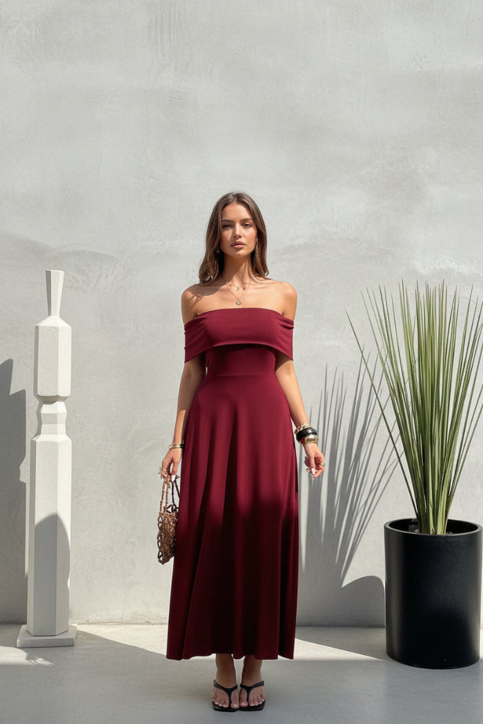 Woman wearing a burgundy off-shoulder dress standing outdoors.