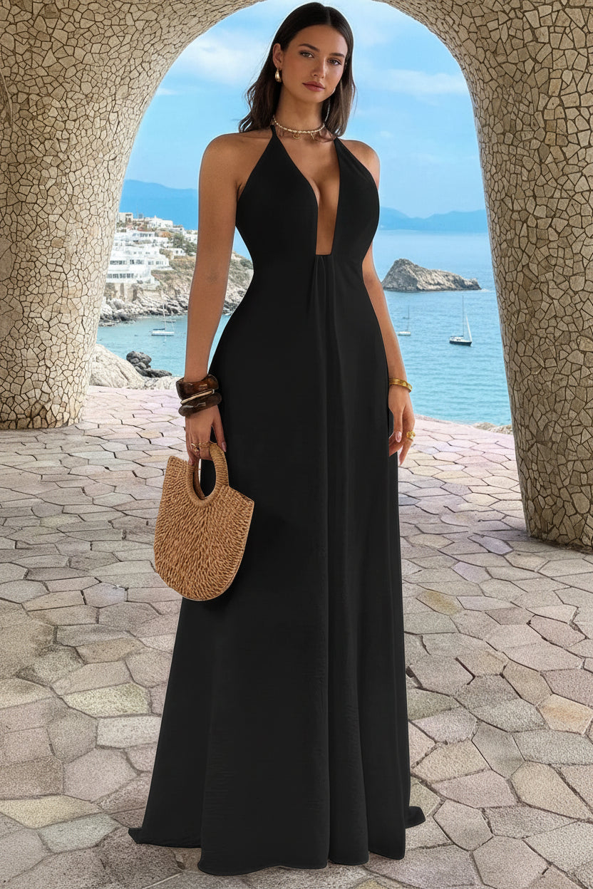 Woman in a black halter neck dress holding a straw bag by the sea.