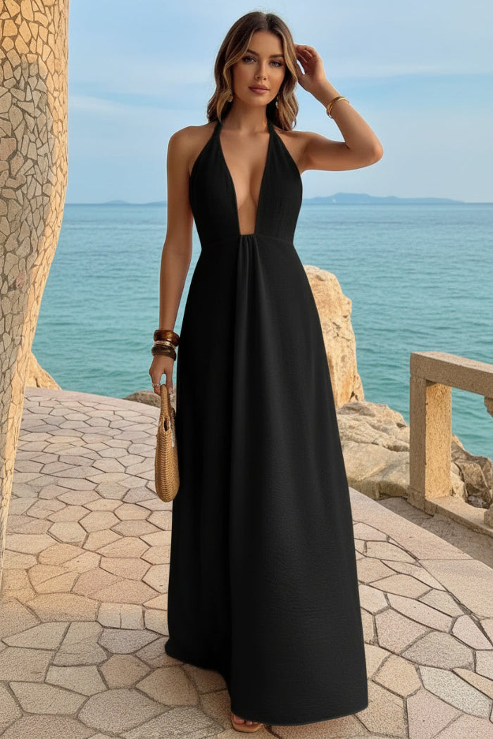 Woman in a black dress standing by a stone wall with ocean view