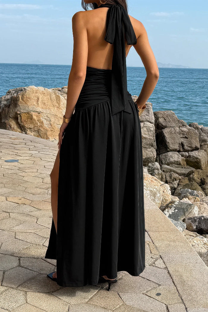 Woman in a black halter neck dress standing by a rocky coastline.