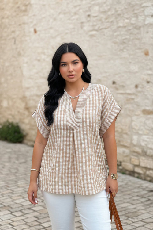 Woman wearing a plaid shirt and white pants with a neutral background