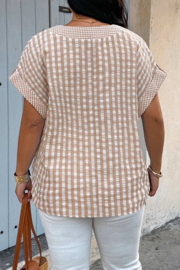 Person wearing a beige and white checkered shirt with white pants, standing against a light-colored wall.