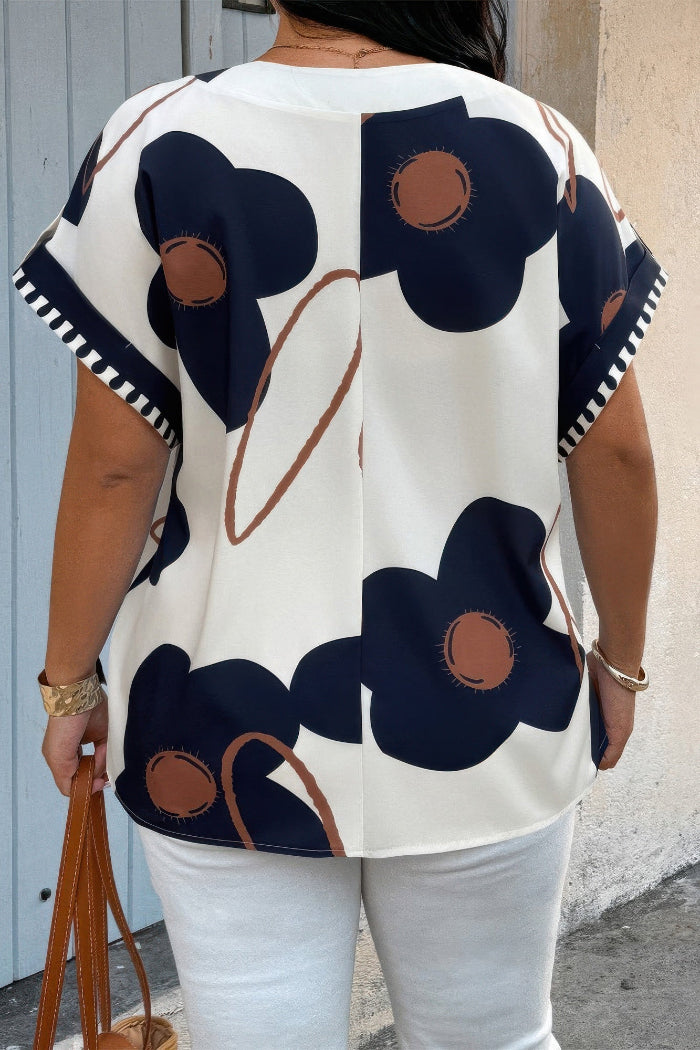 Person wearing a floral patterned top with navy blue flowers and brown centers, standing against a neutral background.