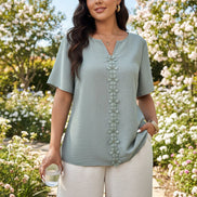 A woman wearing a light sage green short-sleeve top with a V-neck and a vertical row of flower-shaped buttons down the front, 