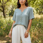 Woman wearing a light gray top with decorative buttons and beige pants indoors.