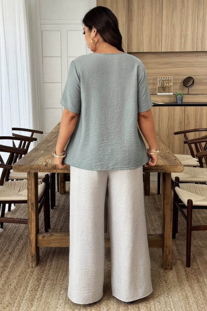 Woman standing at a wooden table in a room with chairs and a mirror.
