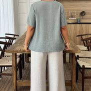 Woman standing at a wooden table in a room with chairs and a mirror.