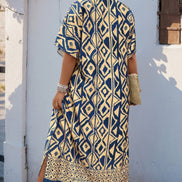 A woman wearing a navy blue and beige geometric print kurta dress, standing outdoors against a white wall with pink flowers.